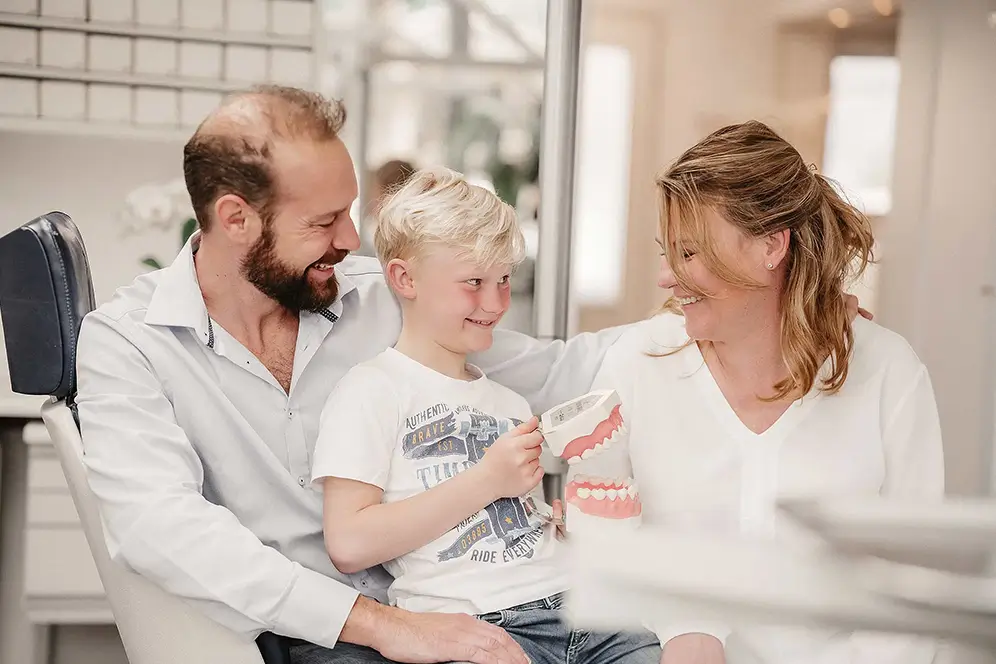 Zahnarzt mit Kind und Mutter in Praxis, Kind hält Zahnmodell zur Beratung